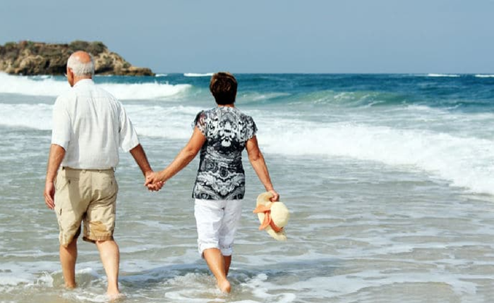 Older vacationing couple walking hand-in-hand on a beach